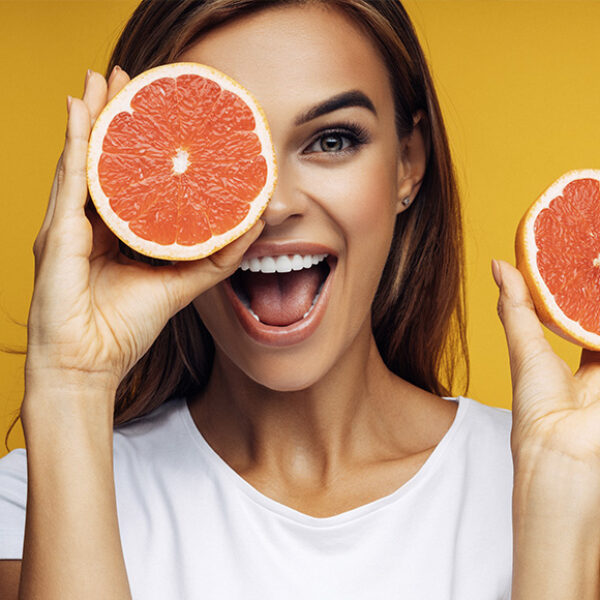 A woman holding a sliced grapefruit up to her face